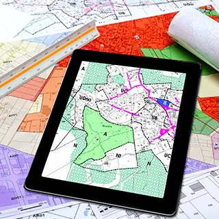 Tablette affichant un plan de zonage, posée sur des plans cadastraux