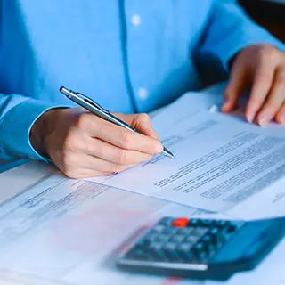 Main remplissant un formulaire au stylo, près d'une calculatrice
