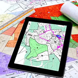 Tablette affichant un plan de zonage, posée sur des plans cadastraux