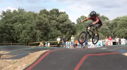Jeune cycliste casqué en plein saut sur une piste de pumptrack, devant des spectateurs