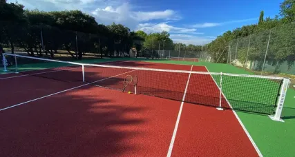 Court de tennis rouge et vert, raquette et balle posées contre le filet