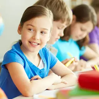 Écolière souriante assise à sa table de classe parmi ses camarades