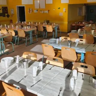 Réfectoire scolaire aux murs jaunes, tables dressées et chaises en bois