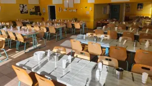 Tables dressées d'un réfectoire scolaire, avec assiettes, couverts et pichets en inox