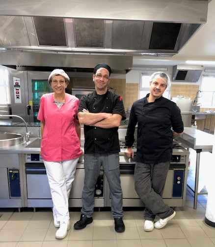 Les trois membres de l'équipe de la restauration scolaire, debout devant les fourneaux de la cuisine
