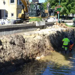 Agents en tenue de chantier au pied d'une berge en travaux, sous une pelleteuse