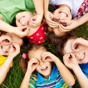 Enfants allongés en cercle dans l'herbe, riant, les mains en lunettes devant les yeux