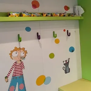 Mur de crèche décoré d'un personnage et d'un chat, patères colorées et étagère verte