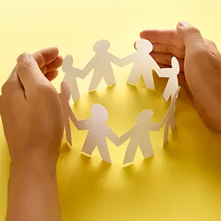 Mains entourant une ronde de personnages en papier découpé