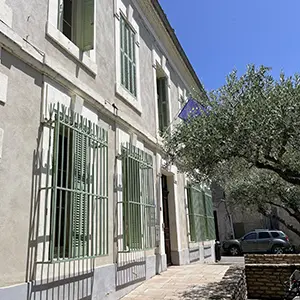 Façade d'un bâtiment public aux fenêtres grillagées, à l'ombre d'un olivier